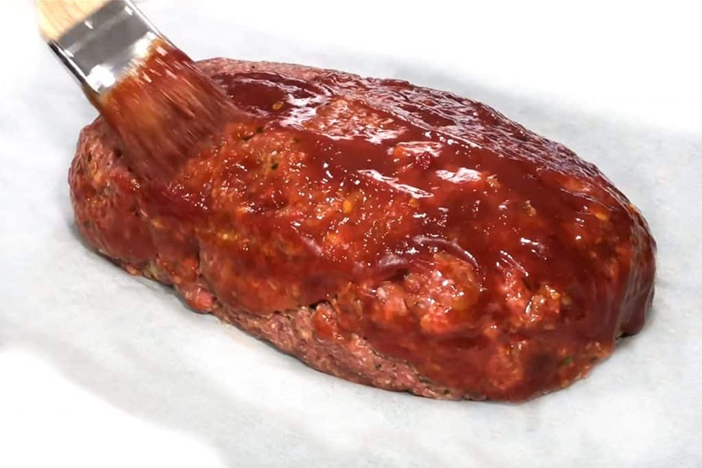 a brush adding the glaze to the raw meatloaf