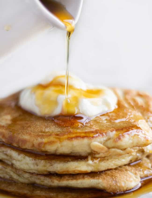 A stack of pancakes on a plate, with Cream and syrup