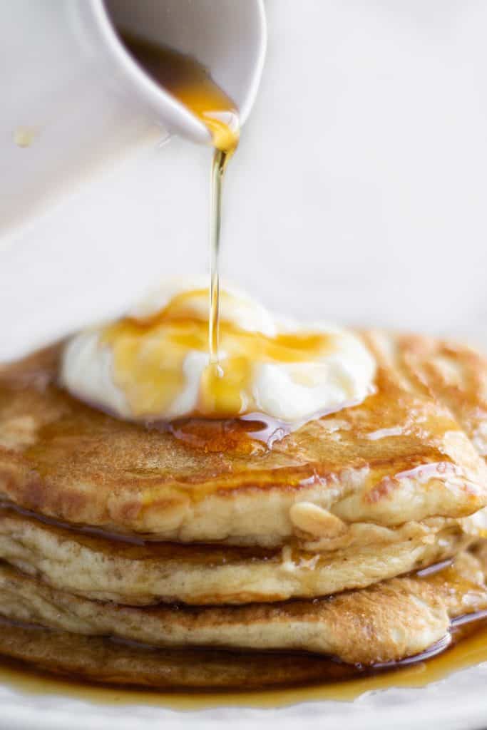 A stack of pancakes on a plate, with Cream and syrup