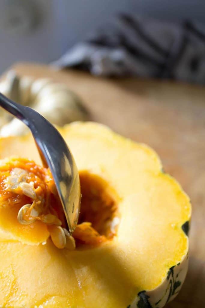 a spoon scraping seeds from the inside of a squash