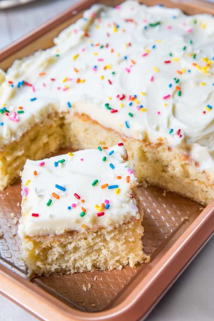 A sheet pan of vanilla cake with a slice cut out of it.