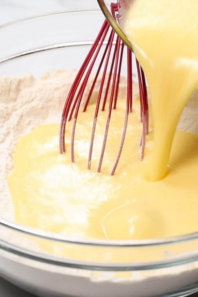 wet ingredients being poured into dry ingredients in a bowl with a whisk