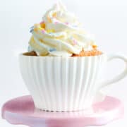 a cupcake on a pink cake stand topped with a swirl of buttercream and decorated with sprinkles.