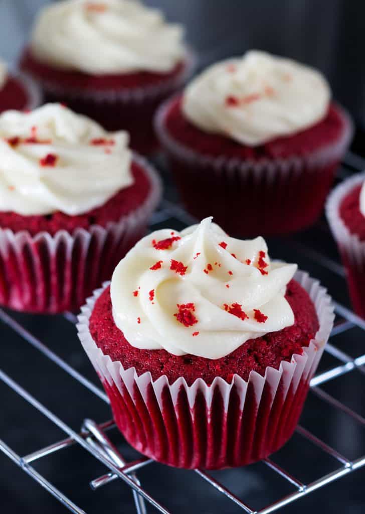 Red Cupcakes swirled with frosting and sprinkled with cake crumbs and more cupcakes in the background.