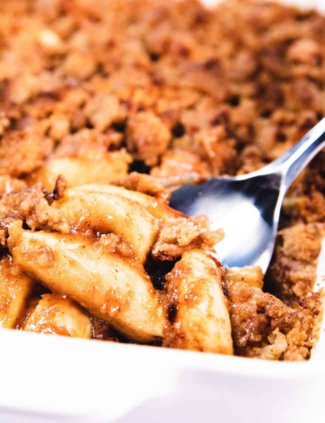 A spoon scooping out a serving of apples with crumb topping