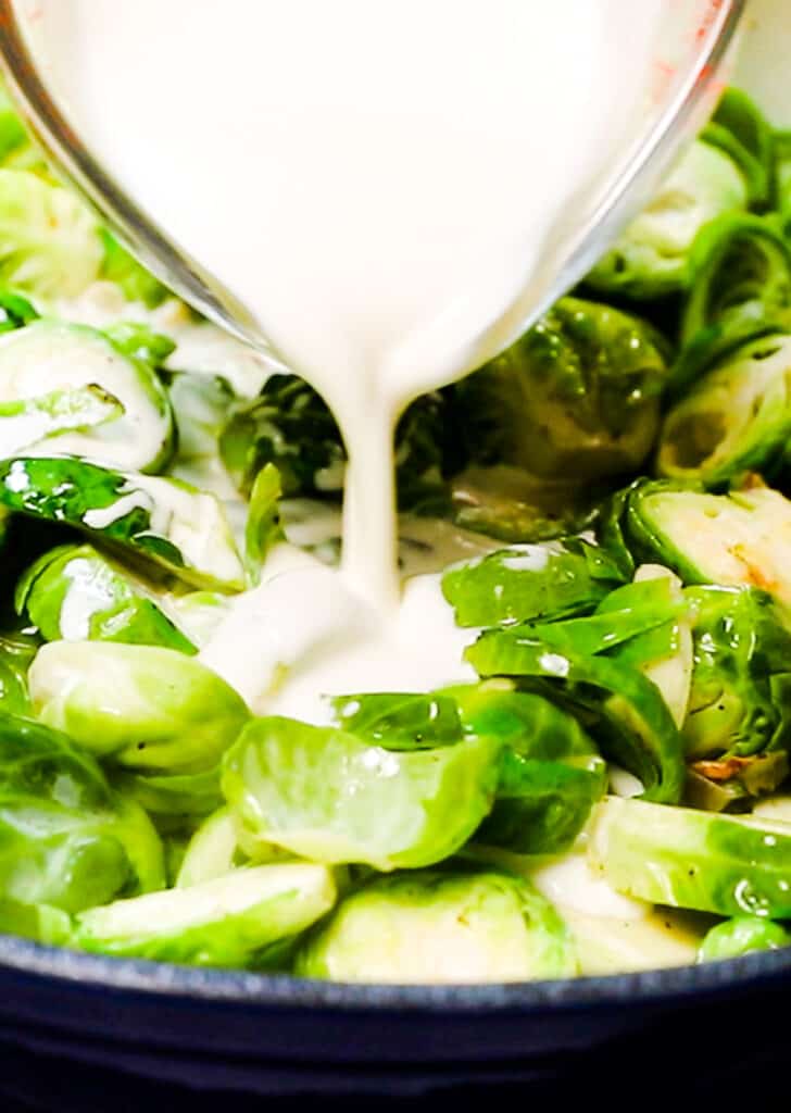 cream being poured over brussels sprouts in pan
