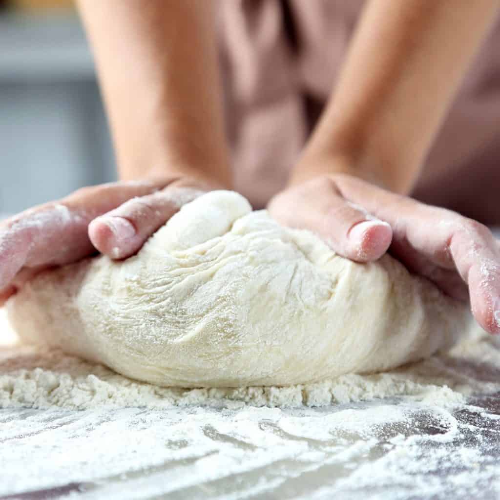 dough being kneaded by hand on a floured surface