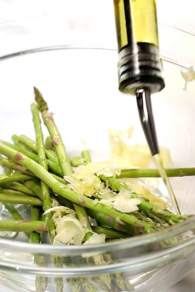 olive oil  being added to a bowl with asparagus