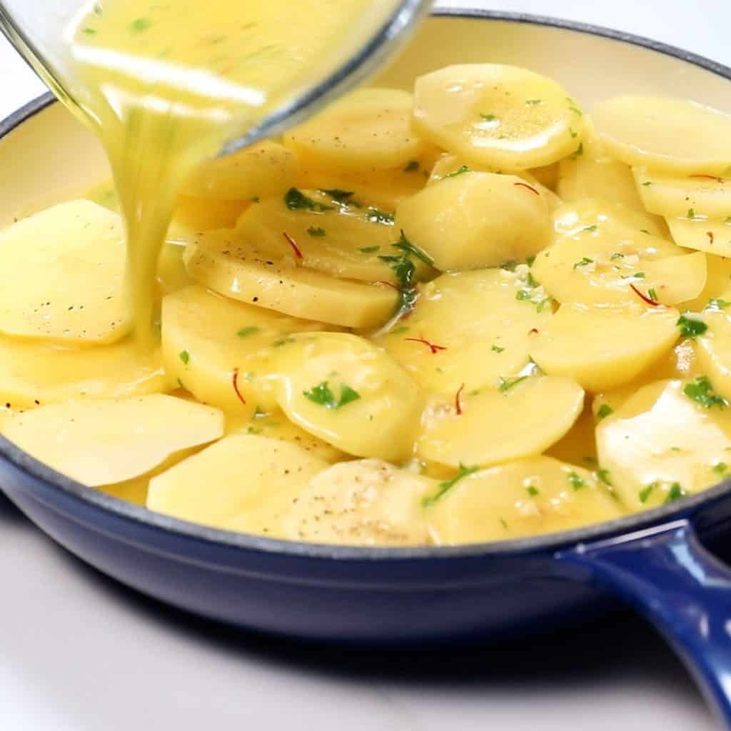 stock mixture being poured over sliced potatoes in a pan