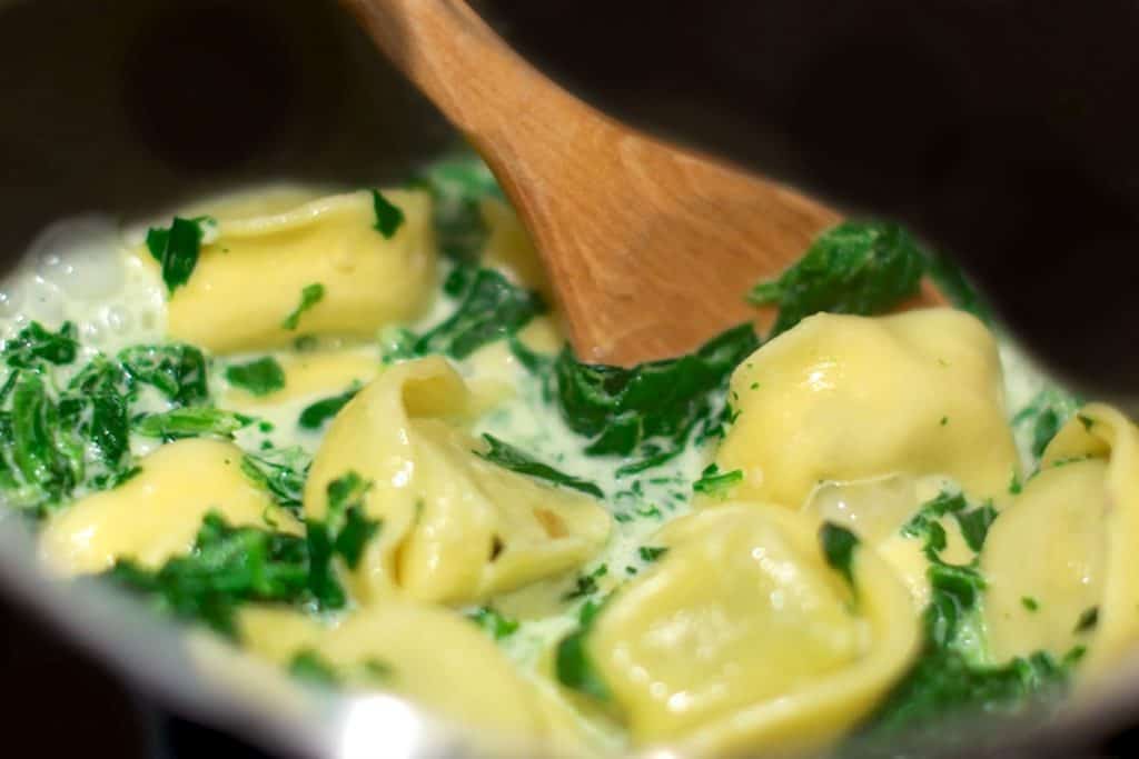 a pan with Tortellini Alfredo and a wooden spoon
