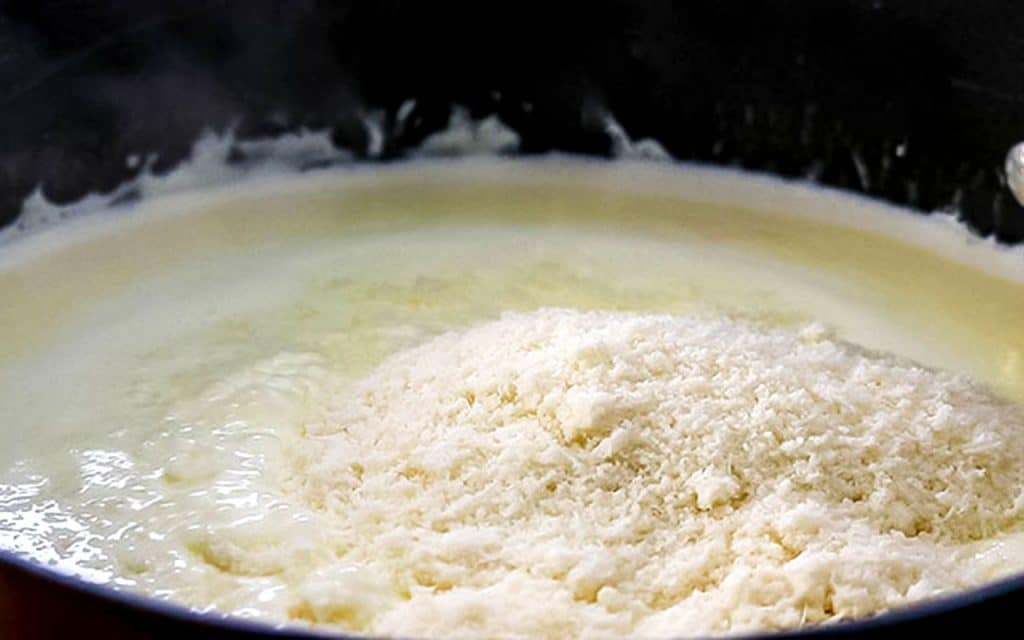 cheese added to alfredo sauce in pan