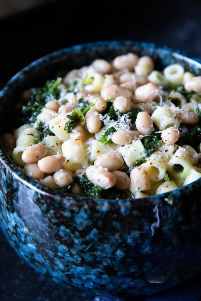 a bowl of white bean soup piled high with pasta and spinach