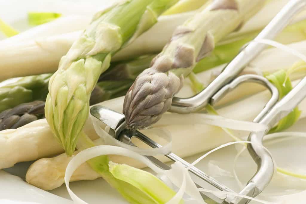 Peeled asparagus with peeler on white background