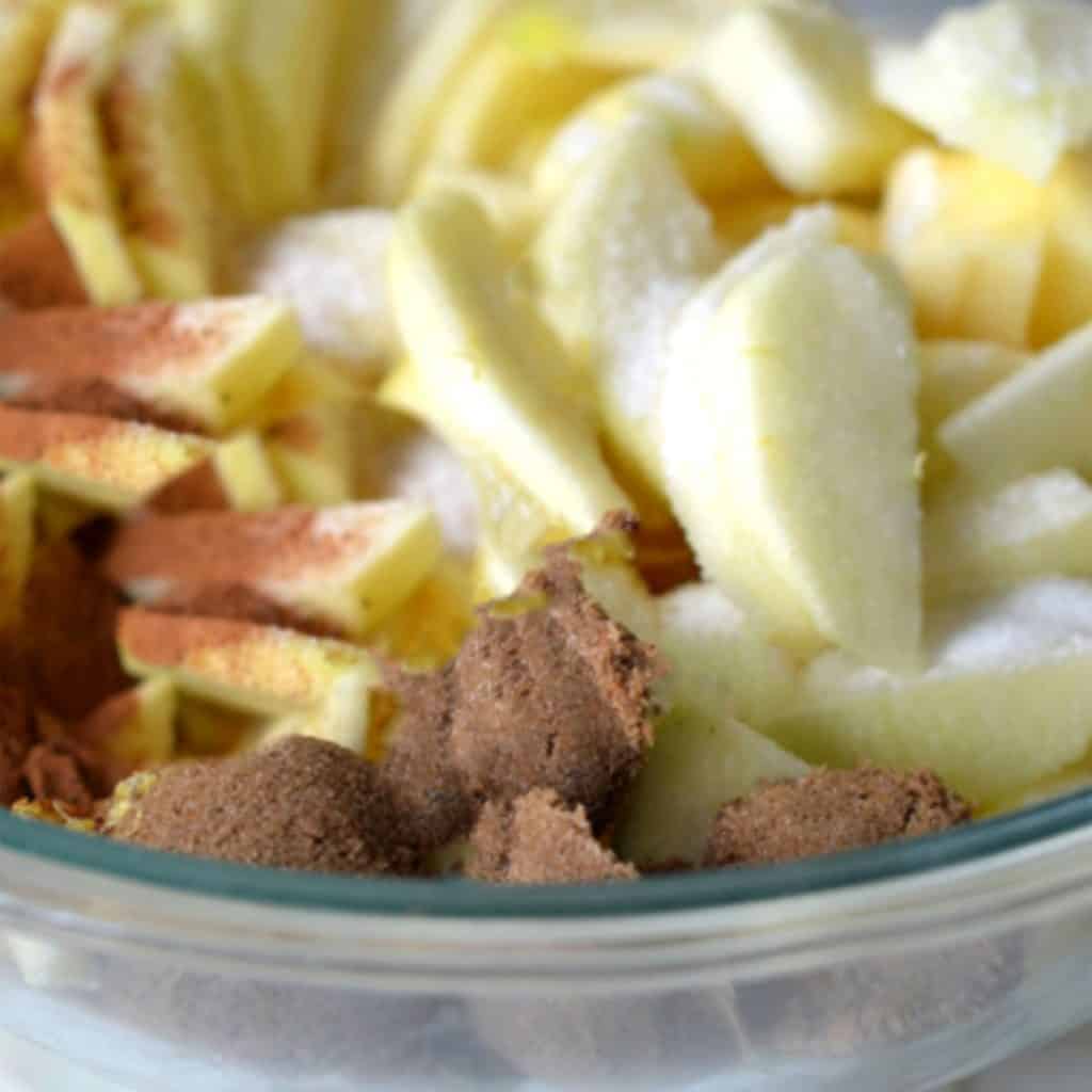 apple slices in a bowl with brown sugar, spices and flour
