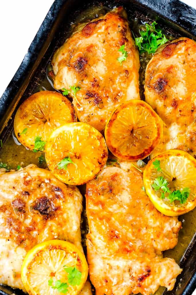 golden chicken breasts in a pan with sauce and lemon slices