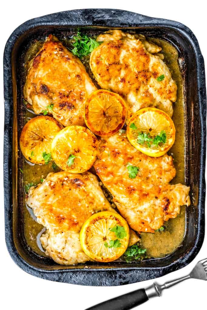 chicken breasts in a serving dish with sauce and lemon slices