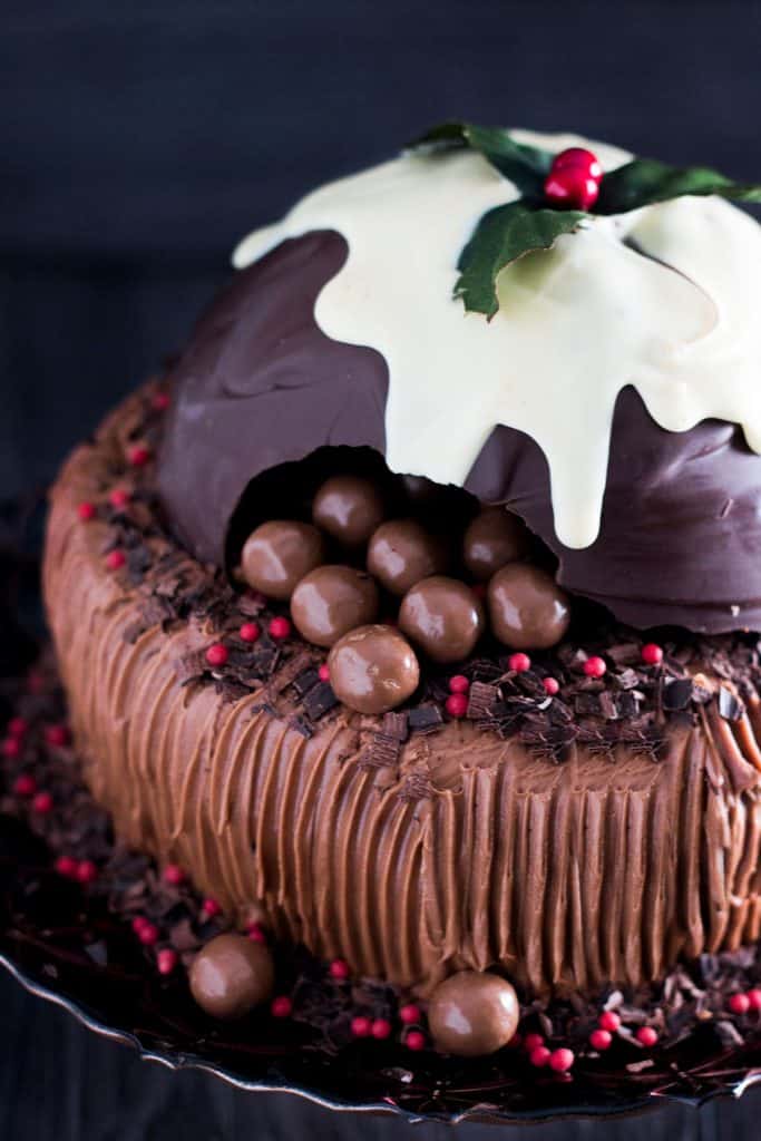 a chocolate cake topped with a christmas pudding made out of chocolate broken open to reveal candy inside