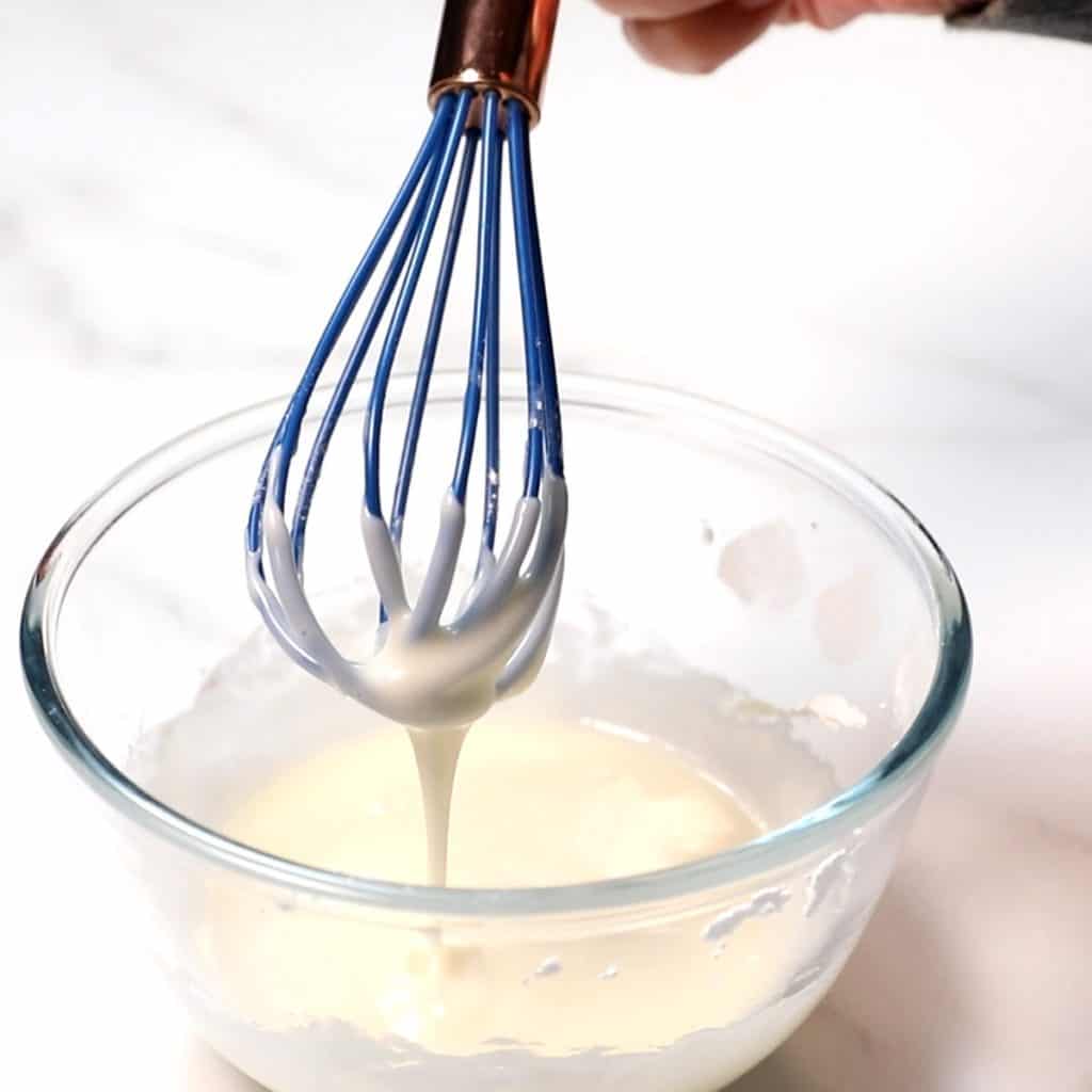 icing dripping from a whisk into a glass bowl.