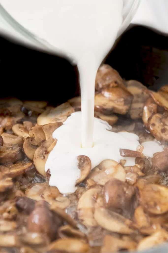 mushrooms in a pan with cream being poured in.