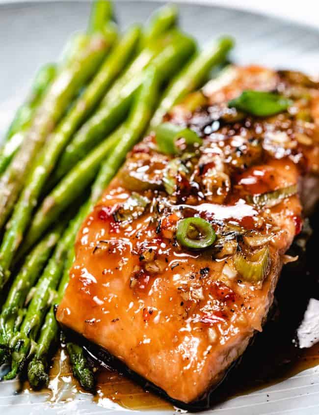 glazed salmon on a plate with asparagus next to it.