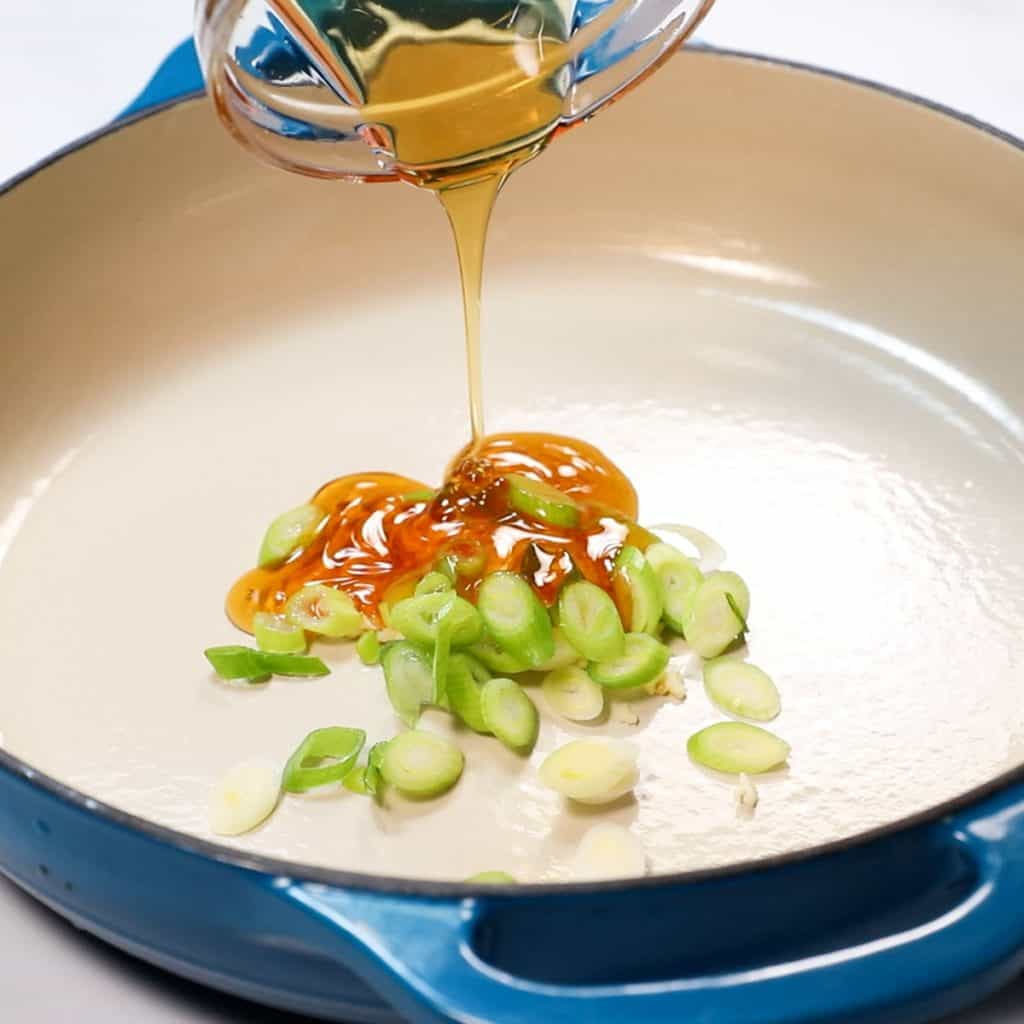 garlic, green onions and honey being poured into a pan