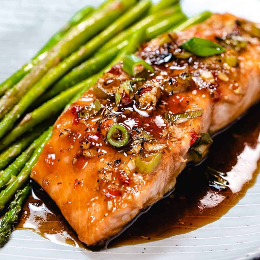 glazed salmon on a plate with asparagus next to it.