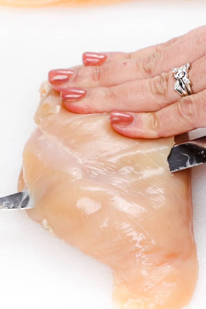 a chicken breast being sliced with a knife.