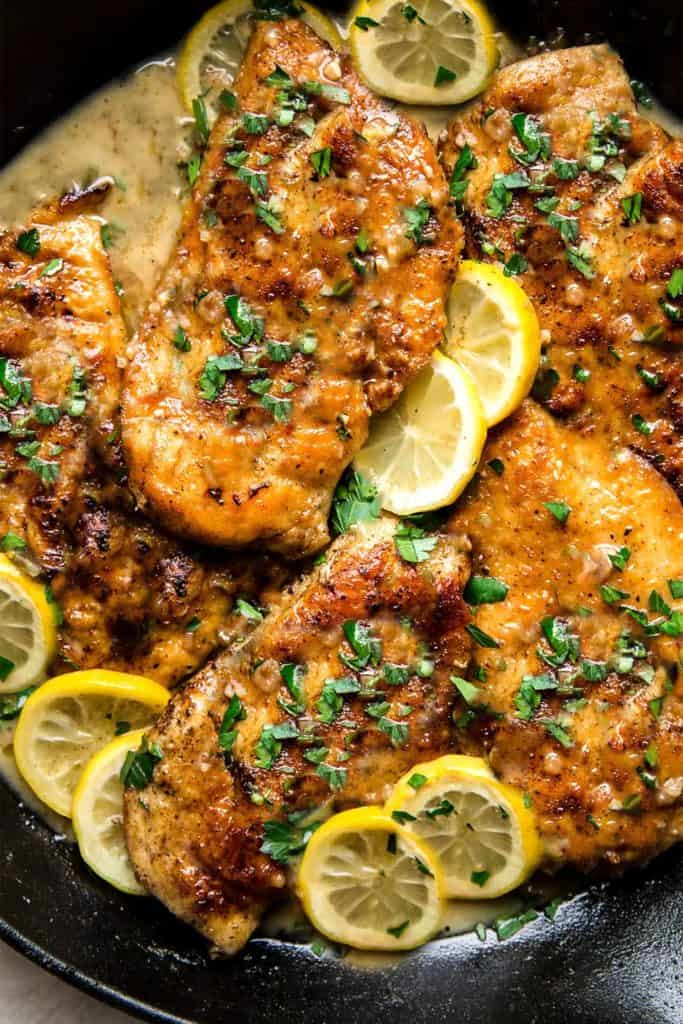 golden chicken breasts in a pan with sauce and lemon slices