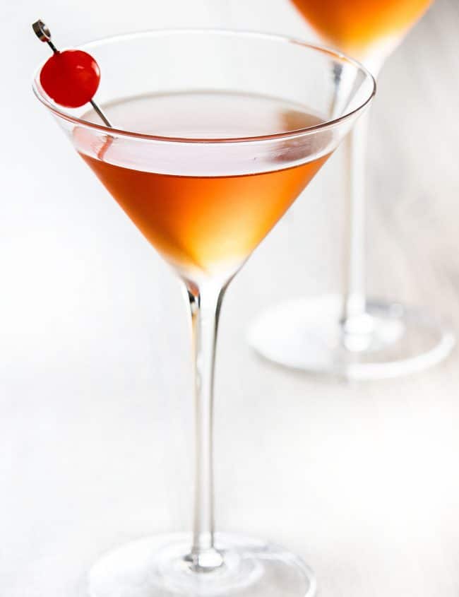 two cocktail glasses with manhattan drink and a cherry