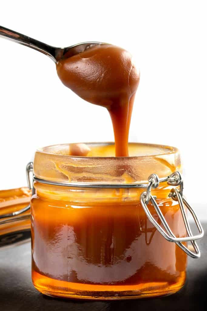 Spoon with tasty caramel sauce over jar on table.