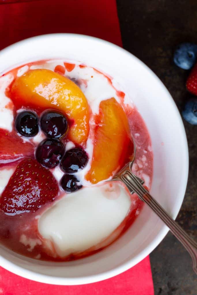 overhead picture of fruit compote and cream in a bowl with a spoon