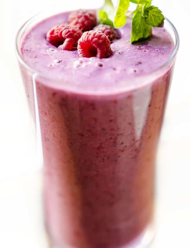 a glass of raspberry smoothie with raspberries and mit