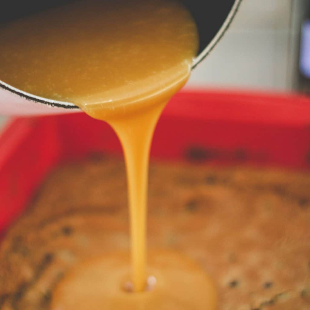 a close up of caramel being poured onto the cooled blondie bar.