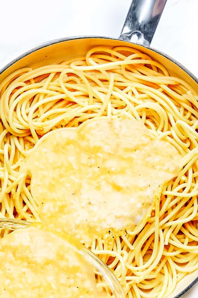 the egg mixture being poured from a bowl into the pan with the spaghetti