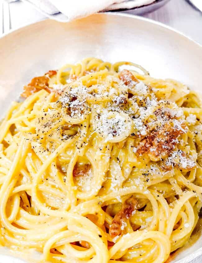 a plate of Spaghetti Alla Carbonara with a basket of bread in the background