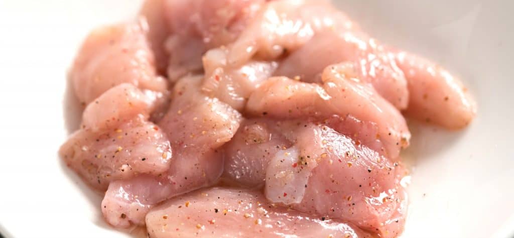 raw sliced chicken fillet meat in spices marinating in bowl