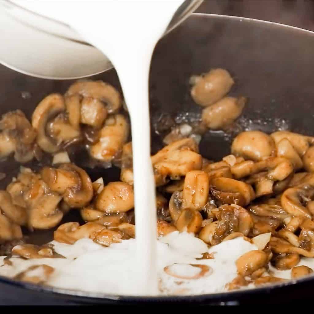 cream being poured over mushrooms in a skillet