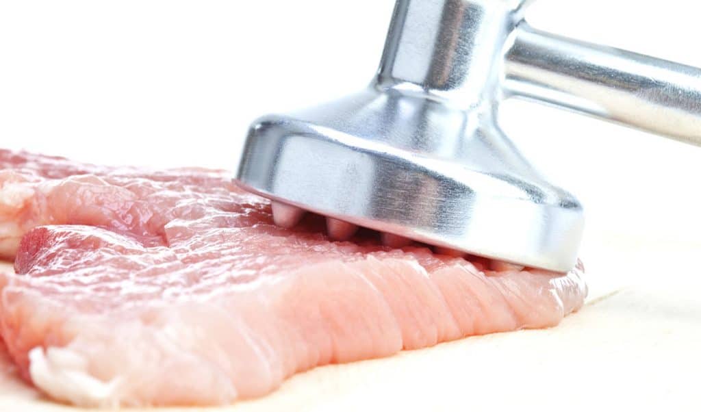 Raw cutlet and meat tenderizer, close-up