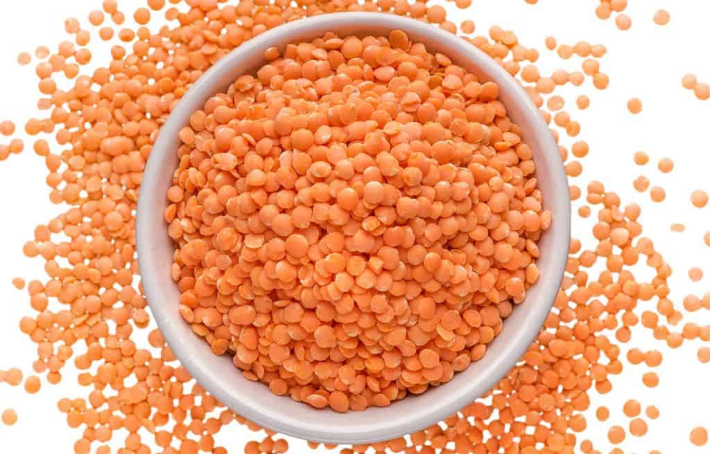 a bowl of red lentils with them scattered on the surface around the bowl