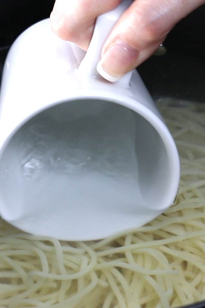 A pot of spaghetti cooking and a mug collecting some water from the pot