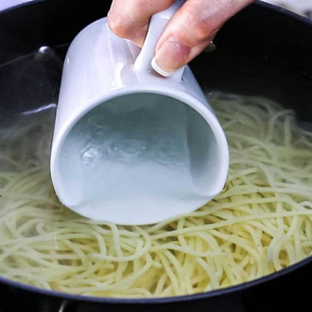 A pot of spaghetti cooking and a mug collecting some water from the pot