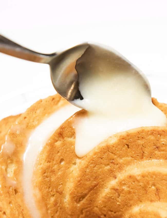 cream cheese glaze being spooned onto a cake