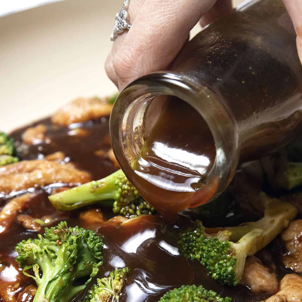 stir fry sauce being poured onto chicken and broccoli