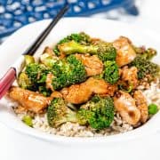 A chicken and Broccoli stir fry piled high on a white plate with chop sticks