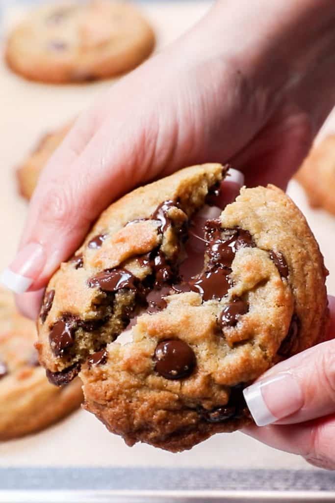a freshly baked cookie being broken open to show melted chips