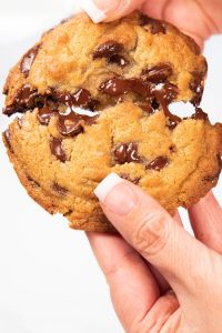 a freshly baked cookie being broken open to show melted chips