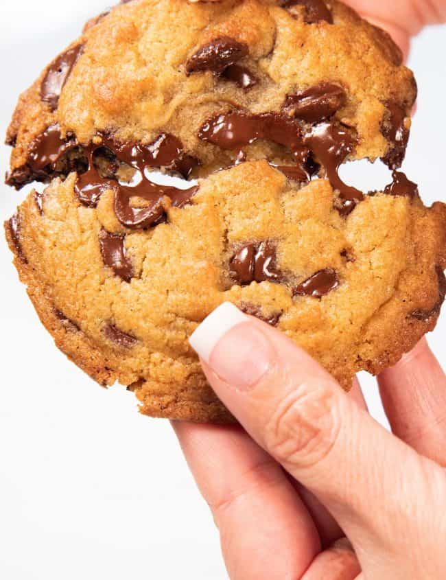 a freshly baked cookie being broken open to show melted chips