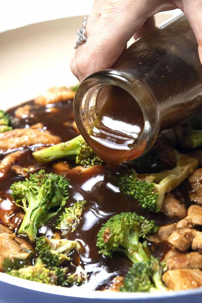 stir fry sauce being poured onto chicken and broccoli