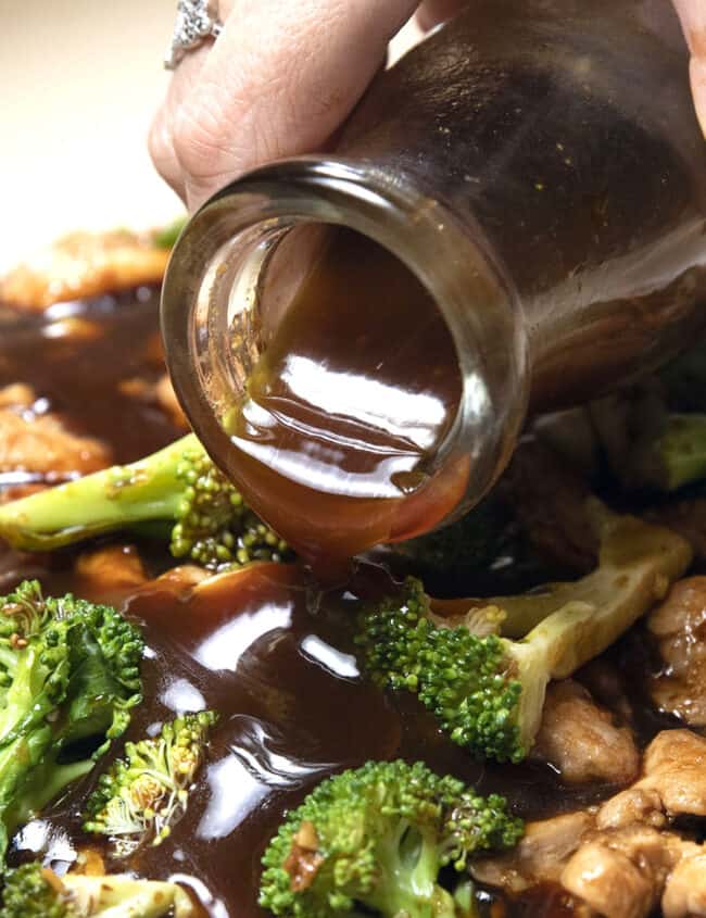 stir fry sauce being poured onto a chicken stir fry in pan