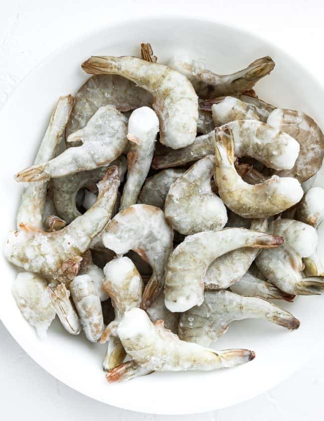 Frozen raw uncooked tiger shrimp on white stone surface, top view flat lay, square format